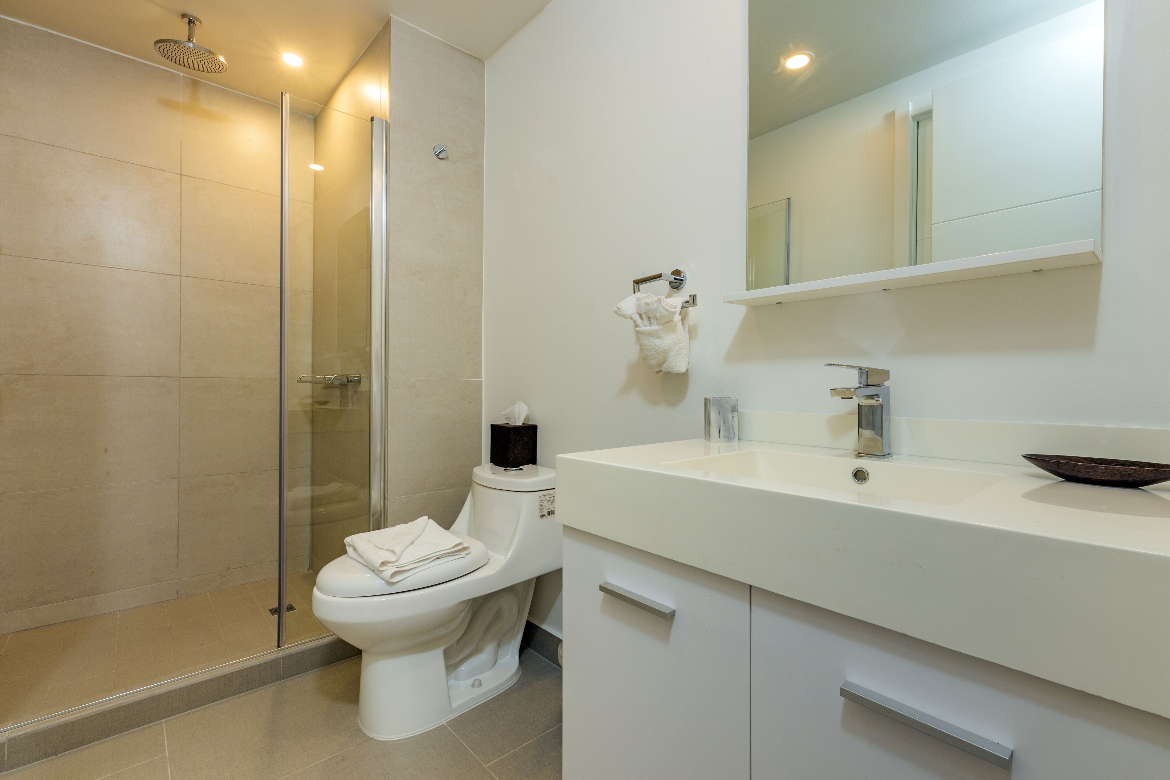 Une salle de bain moderne avec une douche à parois de verre, des toilettes blanches et un meuble-lavabo avec un miroir.