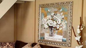 A living room with a brown sofa, patterned cushions, a framed painting of flowers, and a vase with white flowers on the right. - Apartment Ponte Vecchio (Firenze)