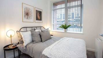 A bedroom with a bed, bedside lamps, a window with blinds, and a radiator.