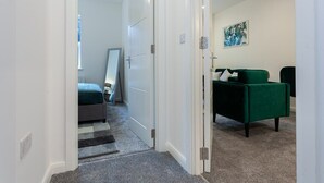 Een gang die leidt naar een slaapkamer met een bed, een groene bank en een schilderij aan de muur.