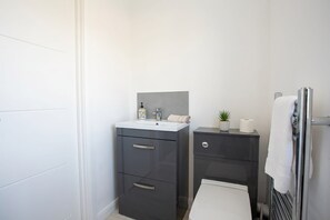Un baño moderno con un lavamanos blanco, muebles oscuros, una planta pequeña y un perchero para toallas.
