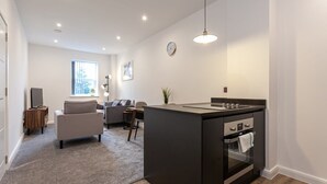 Uma cozinha moderna com uma ilha central, uma sala de jantar com sofá e cadeiras, e uma sala de estar com televisão e janela.