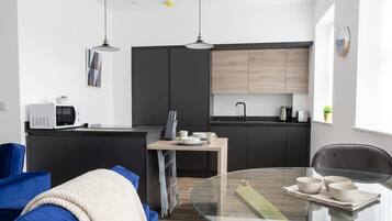 A modern kitchen with dark cabinetry, a microwave, a kettle, and a dining area with a glass table and chairs.
