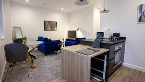 Une cuisine moderne dotée d’un four et d’un micro-ondes encastrés, un coin repas avec des chaises bleues et un petit espace salon avec une table basse et un canapé bleu.