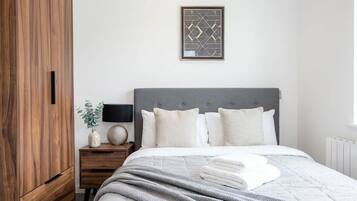 A bedroom with a bed, a nightstand, a lamp, a framed picture, and a wooden wardrobe.