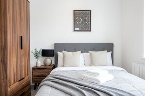 Une chambre à coucher comprenant un lit, une table de chevet, une lampe, un tableau encadré et une armoire en bois.