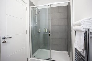 A glass-enclosed shower stall with a white door and tiled walls.