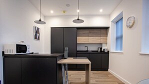 Une cuisine moderne avec des meubles de couleur sombre, un îlot central en bois et des luminaires suspendus.