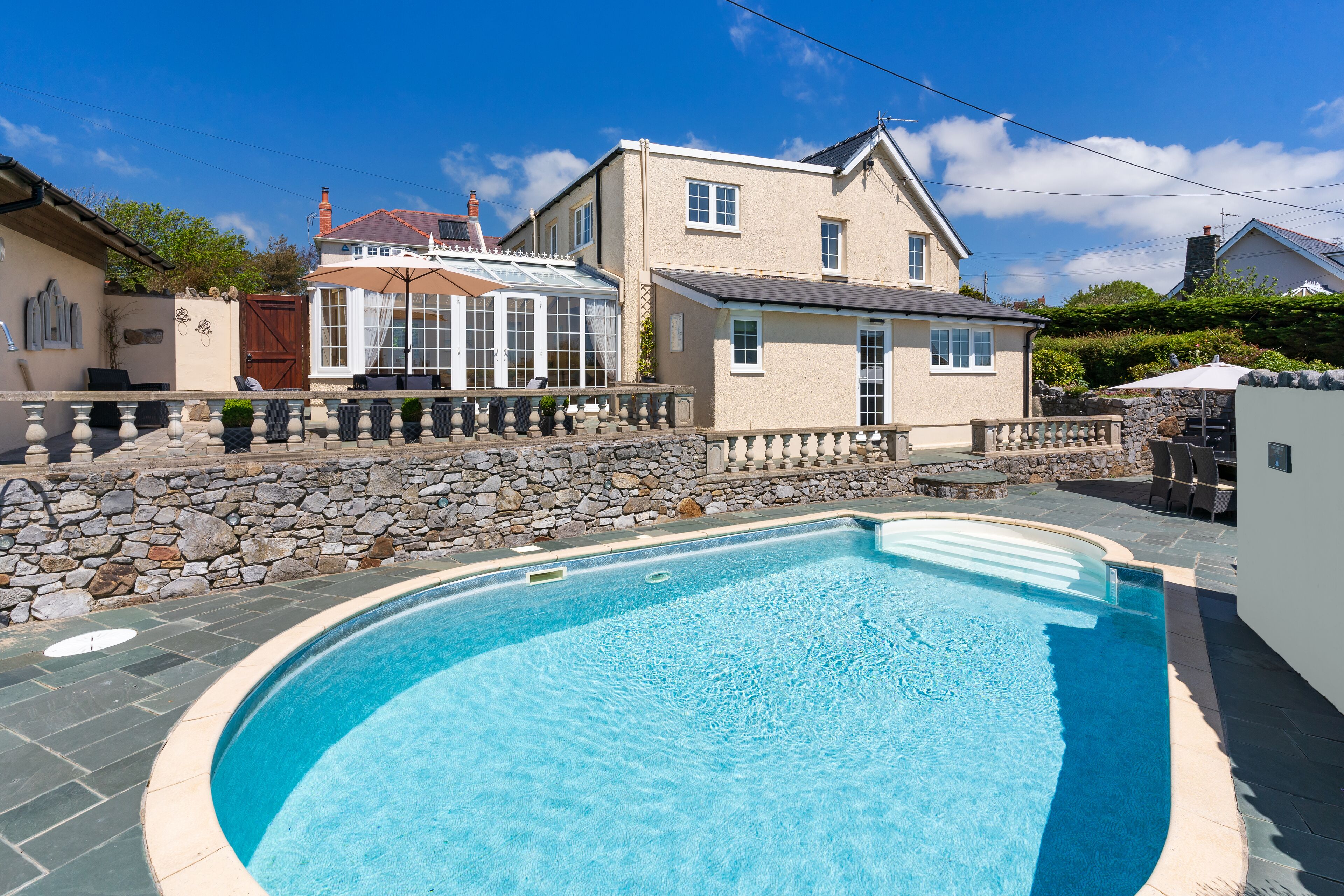 Une piscine avec un mur en pierre et une maison en arrière-plan.