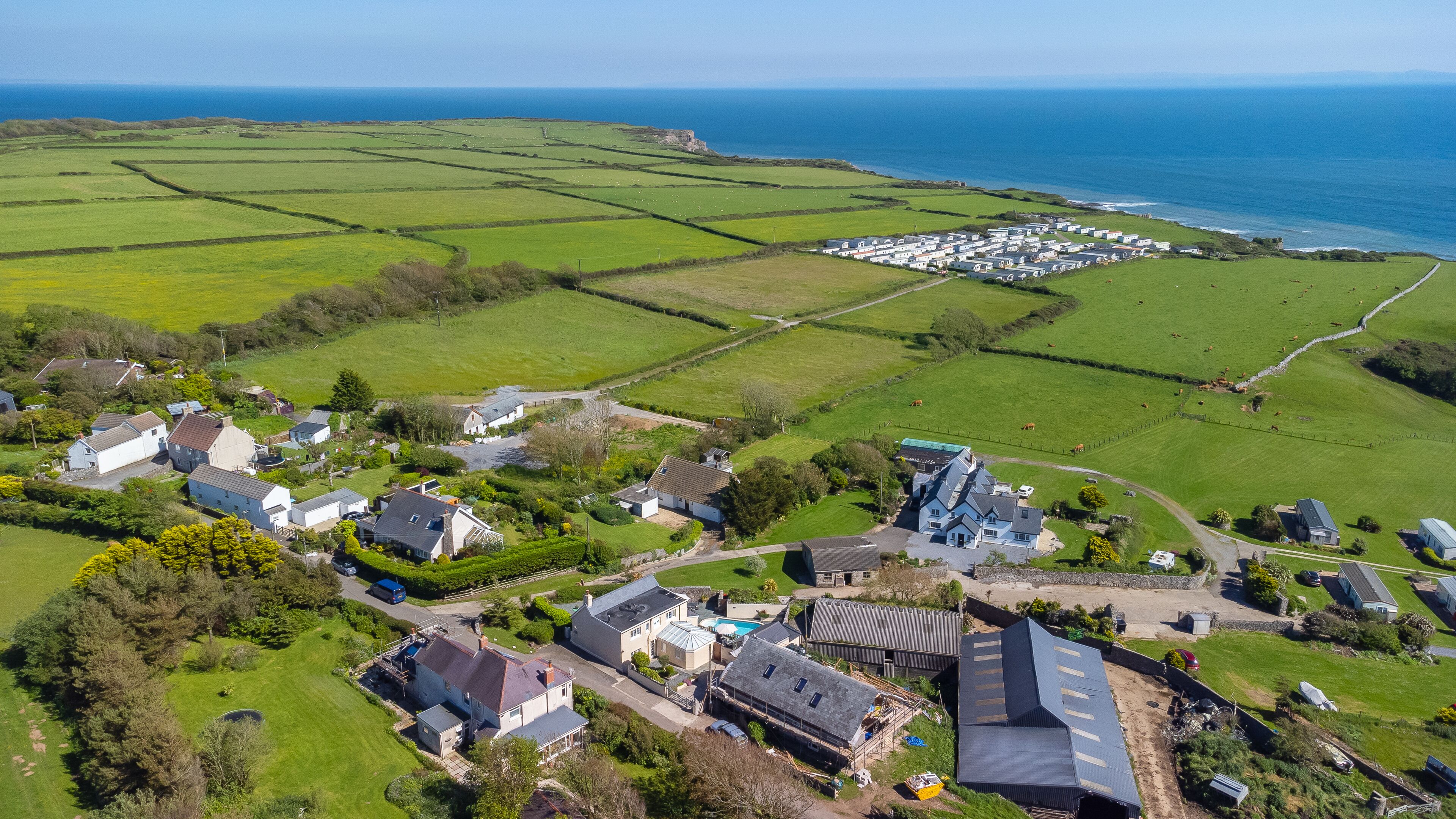 An aerial view of a coastal village with houses, fields, and a caravan park.