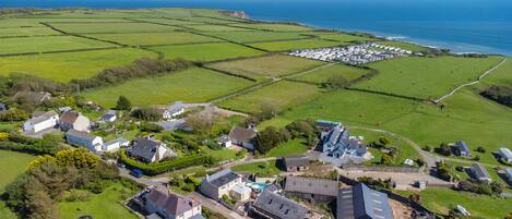 An aerial view of a coastal village with houses, fields, and a caravan park.