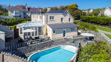 Una casa grande con piscina, un porche cubierto y un muro de piedra alrededor de la piscina.