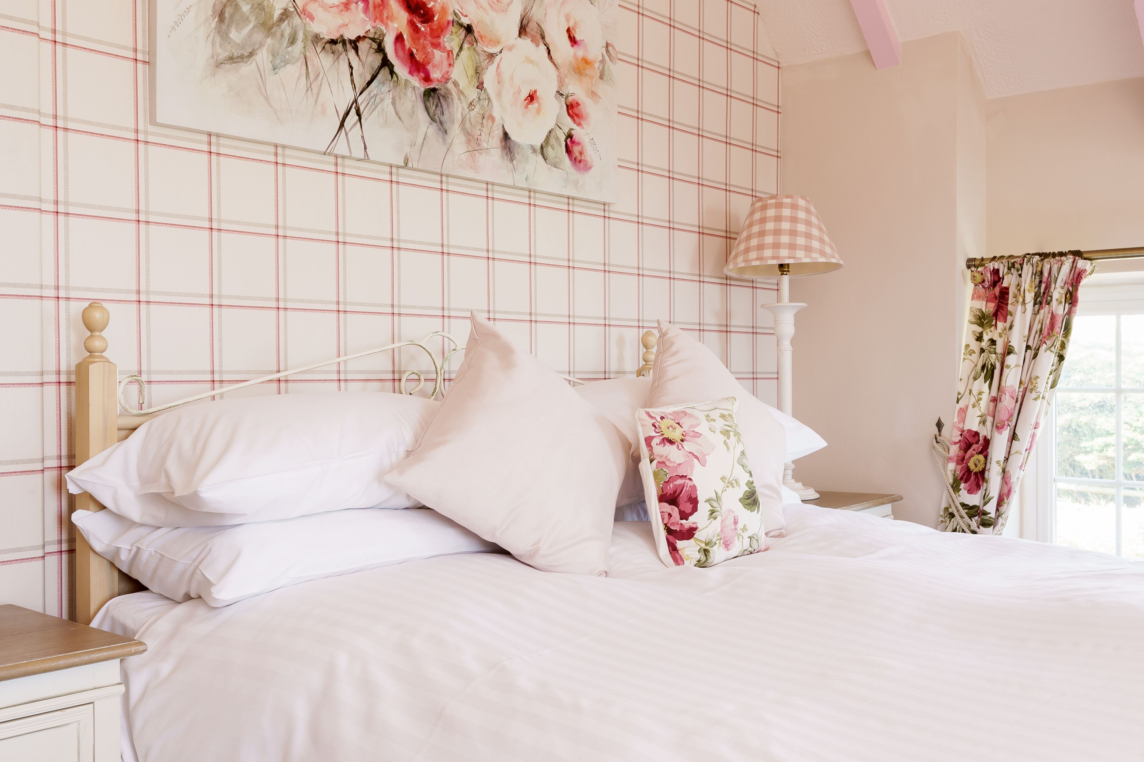 A bedroom with a bed, pillows, a nightstand, a lamp, and a floral painting on the wall.