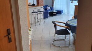 Tilava olohuone, jossa on ruokapöytä ja -tuolit, sininen sohva ja moderni kattokruunu.