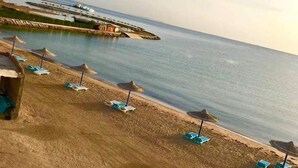 A beach with sun loungers and umbrellas, a pier with boats, and a clear view of the sea. - Cecilia Hurghada (Hurghada)