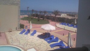 A poolside area with lounge chairs and umbrellas, a clear view of the sea, and a landscaped garden with palm trees. - Cecilia Hurghada (Hurghada)