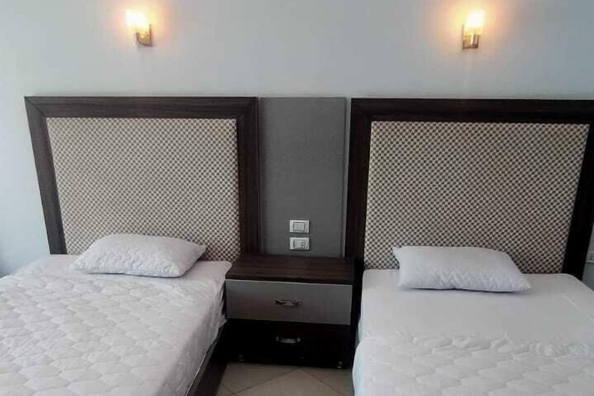 A hotel room with two single beds, each with a headboard and a small bedside table.