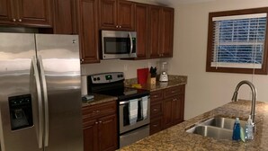 Una cocina con gabinetes de madera, electrodomésticos de acero inoxidable, encimeras de granito y un lavamanos empotrado.