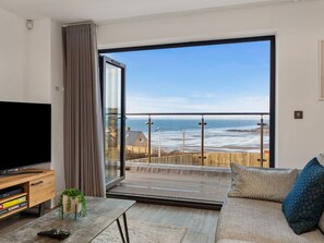Una sala de estar moderna con un amplio ventanal corredera que da a un balcón con vistas a la playa.