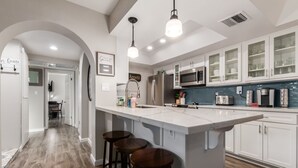Una cocina moderna con una isla grande, taburetes de bar, electrodomésticos de acero inoxidable y armarios blancos.