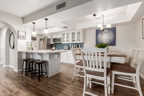 Une cuisine moderne avec des meubles blancs, un îlot central doté de tabourets et des luminaires suspendus.