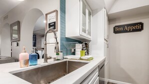 Una cocina moderna con un lavamanos de acero inoxidable, armarios blancos y un letrero que dice 'Bon Appetit' en la pared.