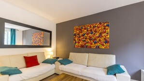 Un salon moderne avec un canapé blanc, des coussins turquoise, une table basse en bois et un tableau abstrait aux couleurs vives accroché au mur.