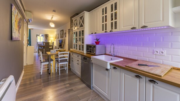Une cuisine moderne avec des meubles blancs, un plan de travail en bois et un éclairage violet sous les meubles hauts.