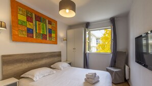 Une chambre d’hôtel avec un lit, une table de chevet, une chaise, un téléviseur et une fenêtre avec des rideaux.