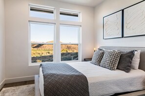 A bedroom with a large bed, a view of a landscape through a window, and two framed artworks on the wall. - Albatross On The 8th: Private Pool And Hot Tub! (Washington)