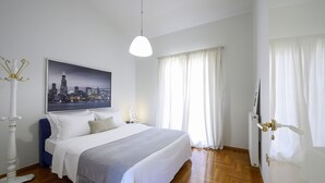 Ett välordnat sovrum med en säng, en målning som föreställer en stadsbild, en vit lampa och en dörr med ett handtag.