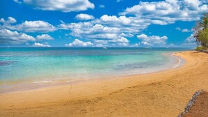 Een strand met helder turquoise water, een zandstrand en een gedeeltelijk bewolkte lucht.
