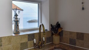 Cuina amb finestra que dona a un cos d'aigua, aixeta d'estil antic i suport per a utensilis.