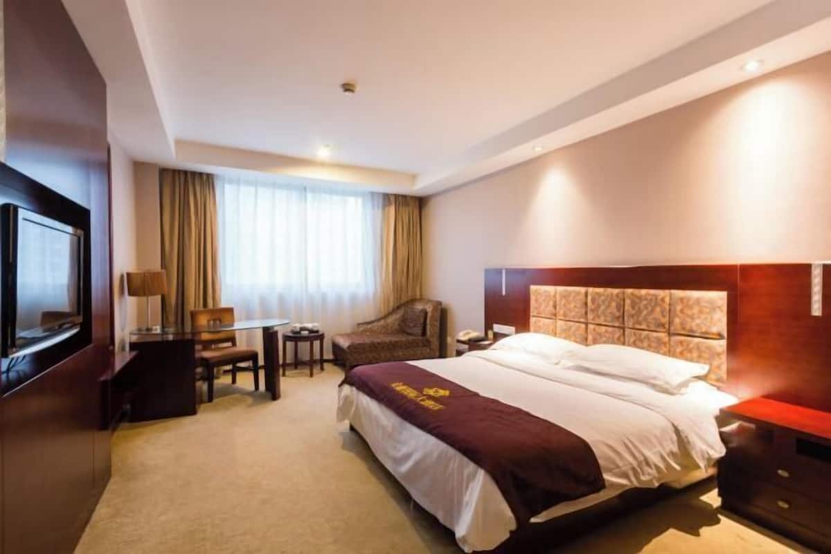 Habitación de hotel con una cama grande, un escritorio, una silla, un televisor y una ventana con cortinas.