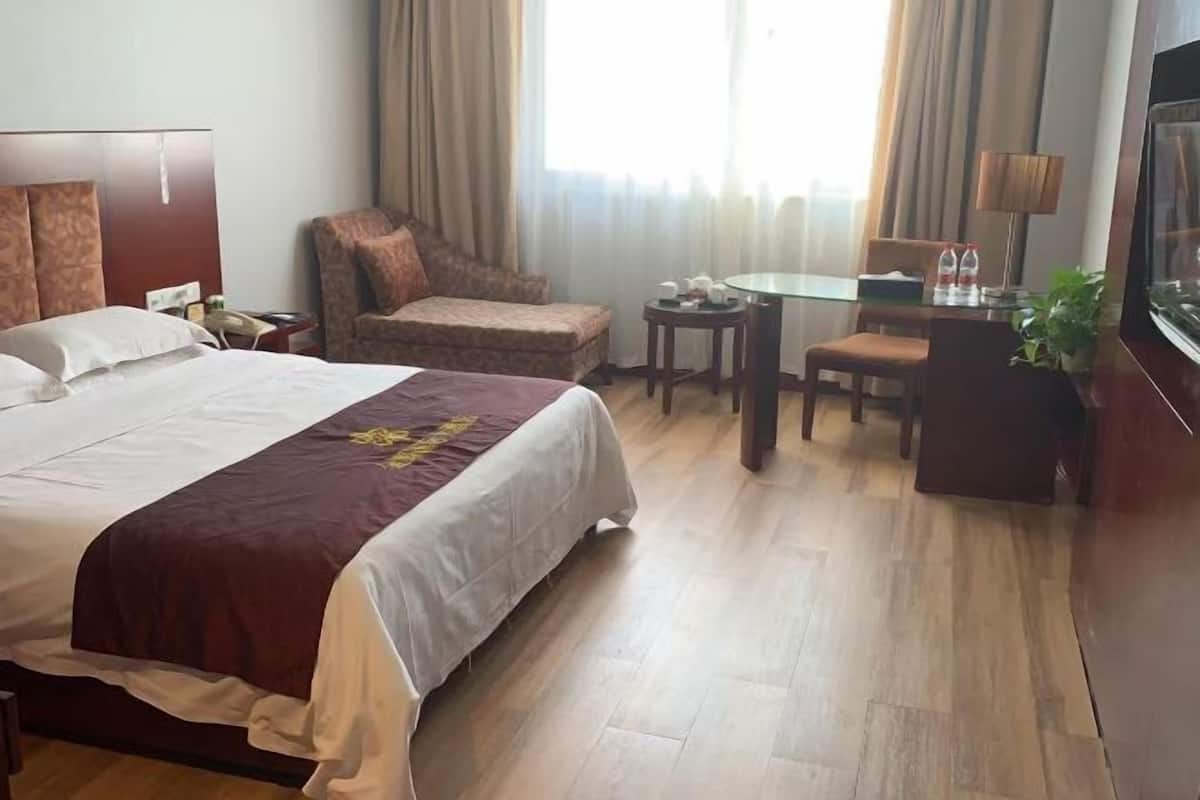 Una habitación de hotel con una cama grande, una silla, una mesita y un televisor.