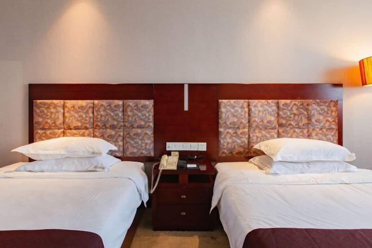 Habitación de hotel con dos camas, cabecera de madera, mesita de noche con teléfono y lámpara fijada a la pared.