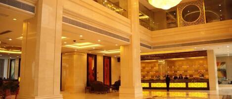 A spacious lobby with high ceilings, a grand chandelier, and a reception desk.