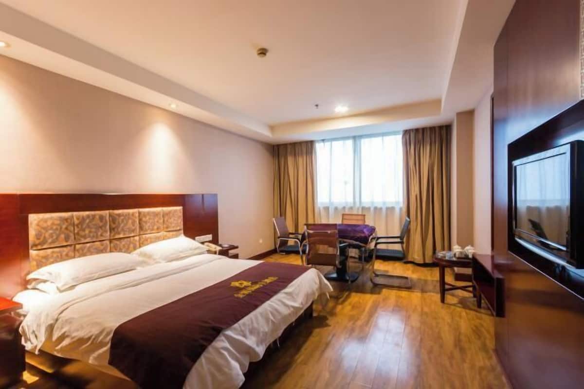Una habitación de hotel con una cama grande, un escritorio, una silla, un televisor y una ventana con cortinas.