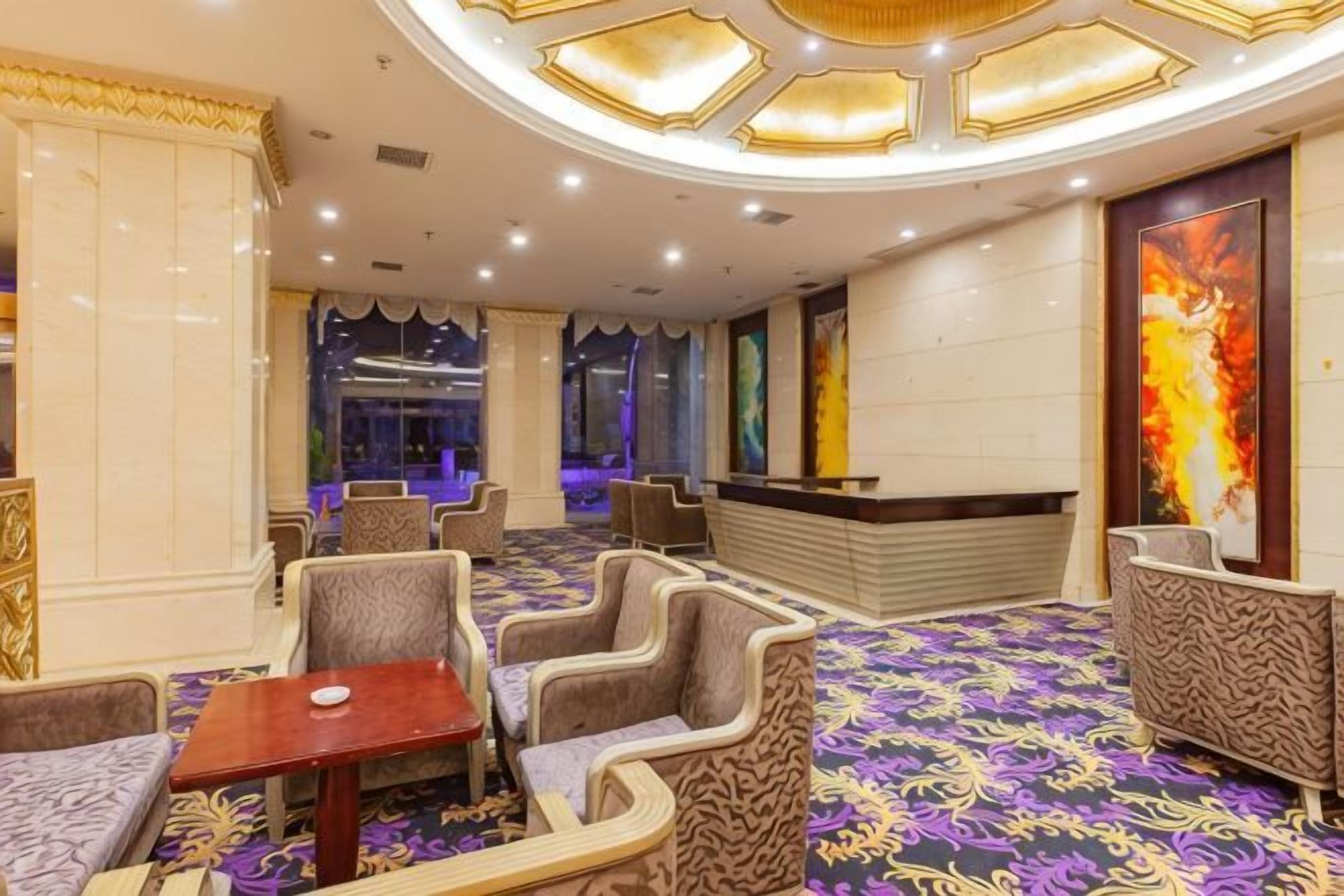 A hotel lobby with a reception desk, seating area, and a patterned carpet.