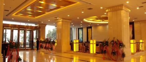 Un hall de hotel con piso pulido, amplias columnas y mostrador de recepción.