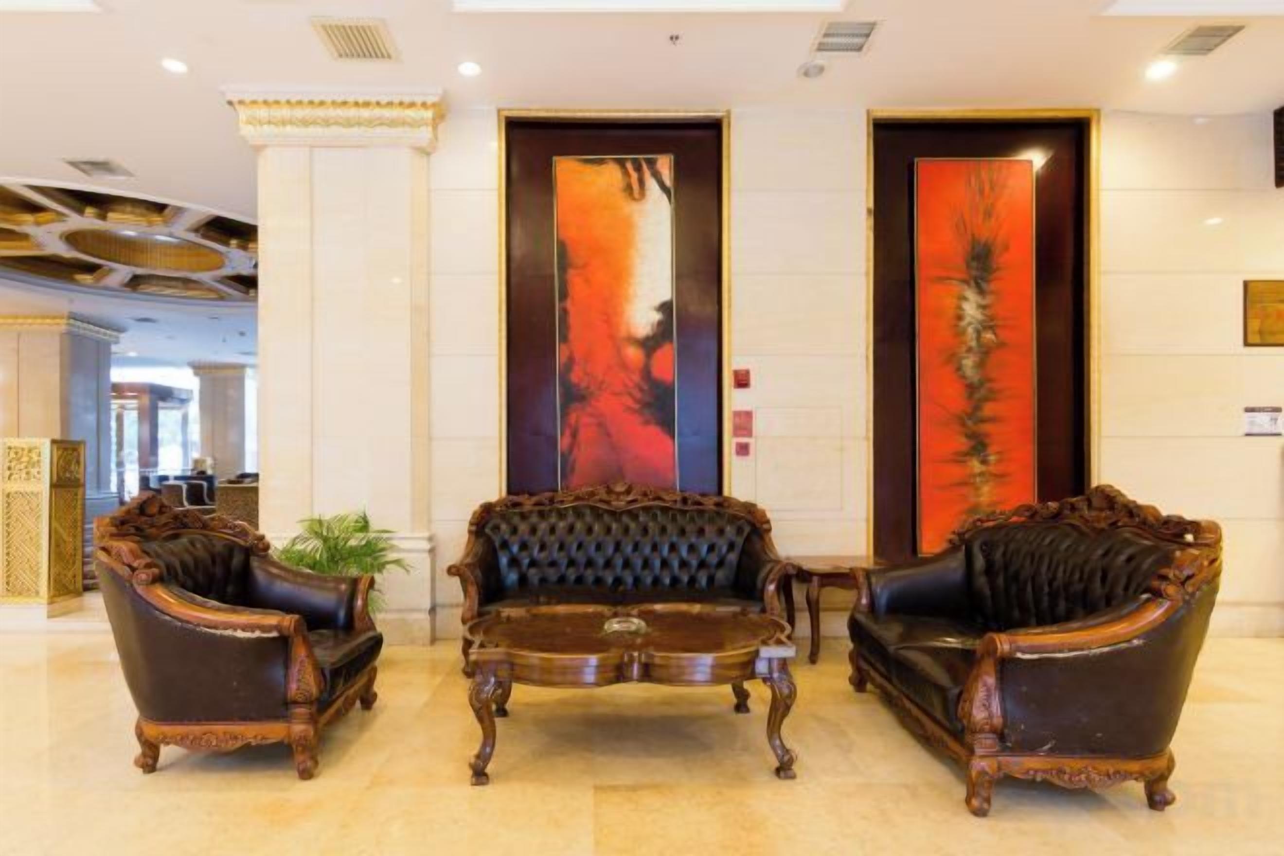 A lobby with three ornate armchairs and a central coffee table, a large vertical painting on the wall, and a reception desk in the background.