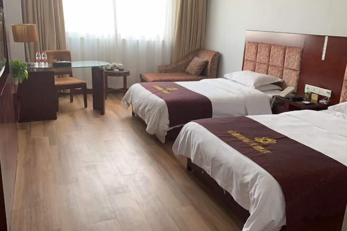 Habitación de hotel con dos camas, un escritorio, una silla y una mesita.