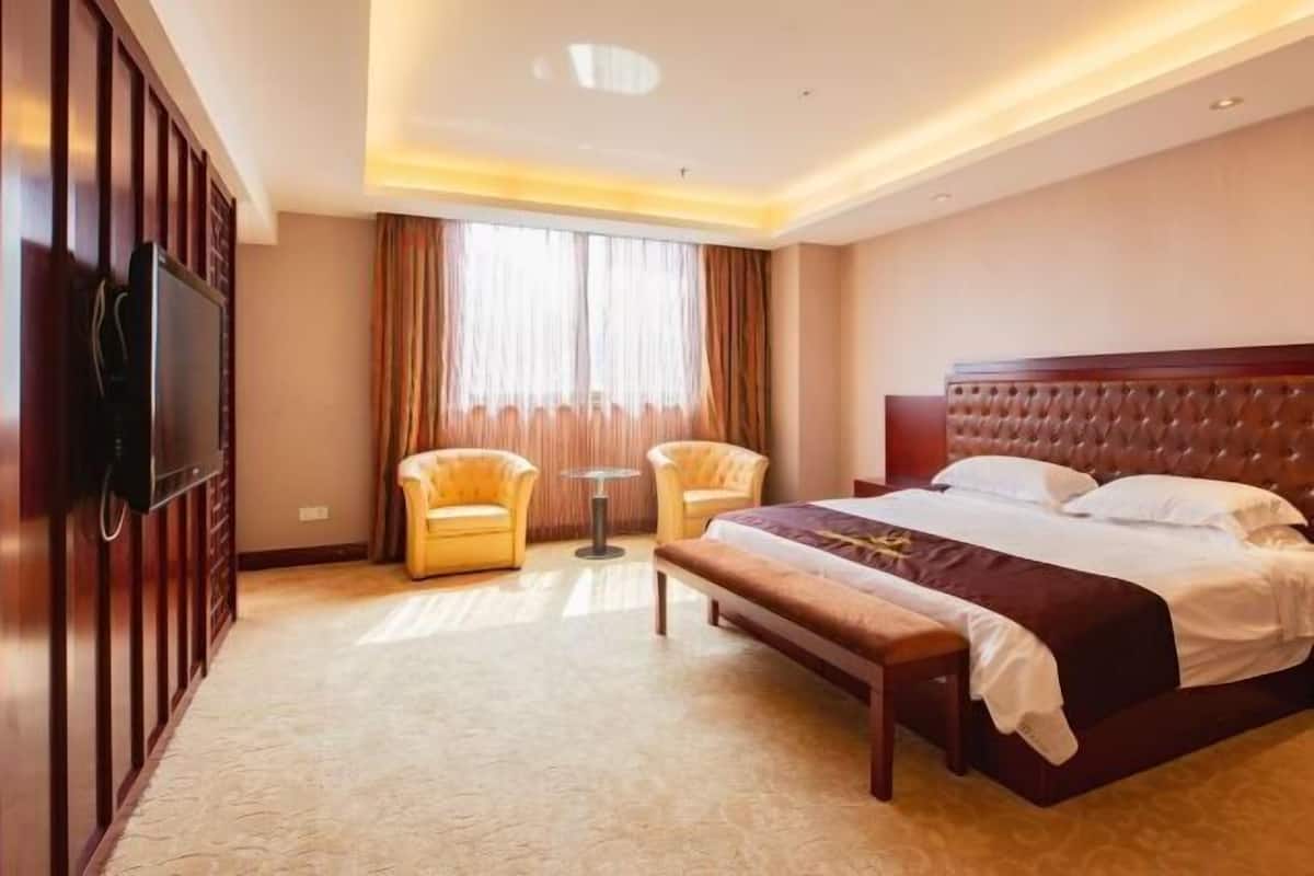 Una habitación de hotel con una cama, dos sillones, una mesita y un televisor montado en la pared.