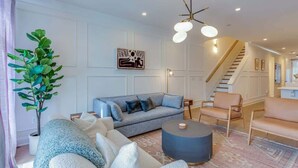 A modern living room with a grey sofa, a round coffee table, and a staircase leading to an upper level. - Belmont Music Row 4 Bed, Rooftop, 10 Minutes To DT | 24 Hour Hospitality Team, Perfect for Groups, 7.5 Miles to Airport (Nashville)