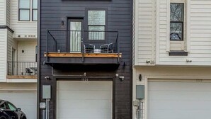A modern two-story building with a garage, a balcony with chairs, and a small outdoor seating area. - Belmont Music Row 4 Bed, Rooftop, 10 Minutes To DT | 24 Hour Hospitality Team, Perfect for Groups, 7.5 Miles to Airport (Nashville)