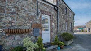 A stone building with a white door, a sign reading "The Bankhouse," and potted plants in front. - Bunk House - 4 Bedroom - Llangenith (Swansea)