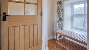 A wooden door with a glass panel, a window with a leaf-patterned curtain, and a wooden shelf unit. - Bunk House - 4 Bedroom - Llangenith (Swansea)