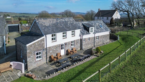 A stone house with a sloped roof, a patio with outdoor seating, and a fenced yard. - Bunk House - 4 Bedroom - Llangenith (Swansea)
