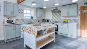 A modern kitchen with light green cabinets, a wooden beam ceiling, and a tiled backsplash. - Bunk House - 4 Bedroom - Llangenith (Swansea)