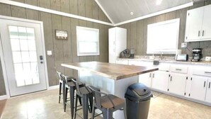 A kitchen with a wooden island, bar stools, white cabinets, and a trash can. - Sugarwood Boathouse (Ten Mile)